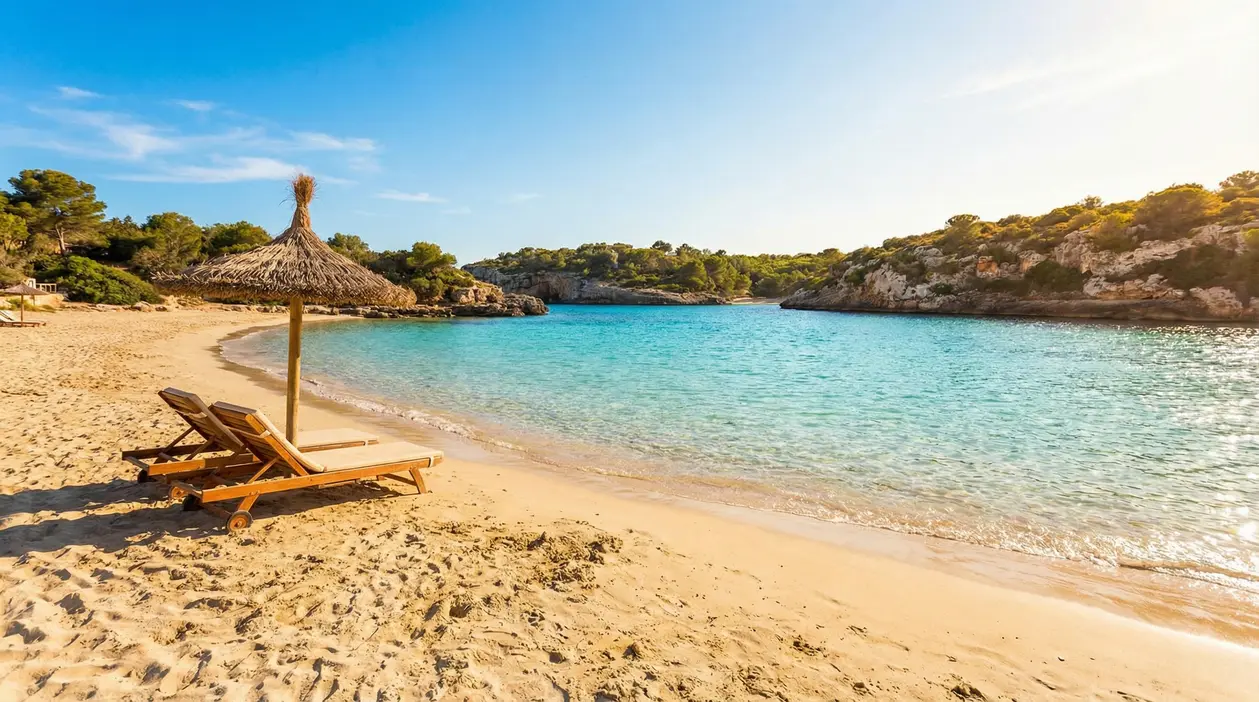 Spiaggia tranquilla con due lettini sotto un ombrellone di paglia e mare turchese