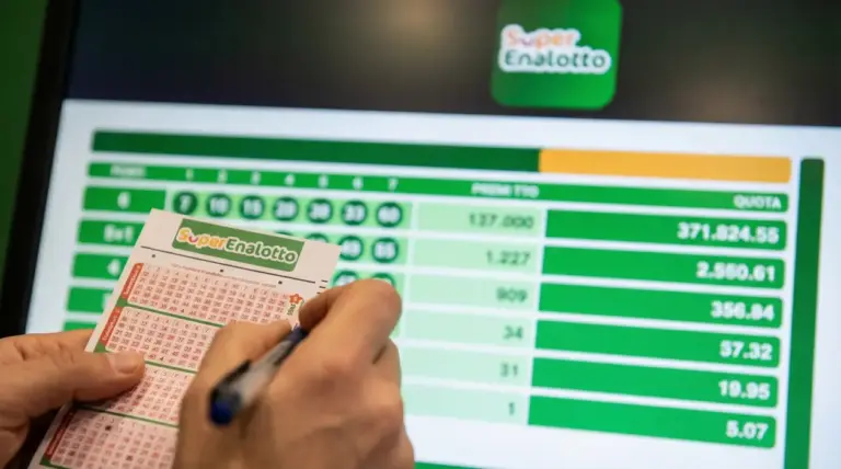 Una persona compila una schedina del Superenalotto davanti a uno schermo con dati delle vincite